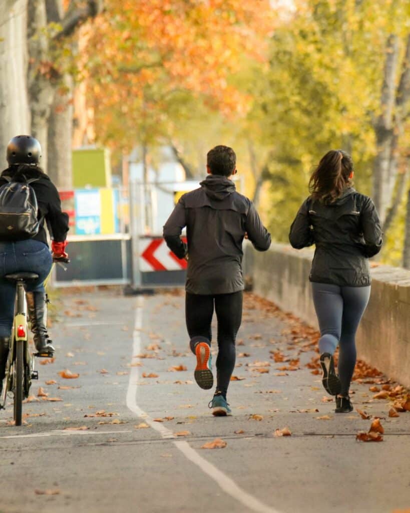 Deux personnes courant et une personne à vélo sur un chemin en ville